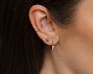 Close-up of an ear styled with Tish Lyon gold star stud and hoop earrings, used to promote piercing services at John Lewis, Oxford Street.