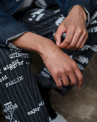 Close-up of a minimalist Tish Lyon gold bracelet worn on the wrist, styled with graphic monochrome trousers and layered denim