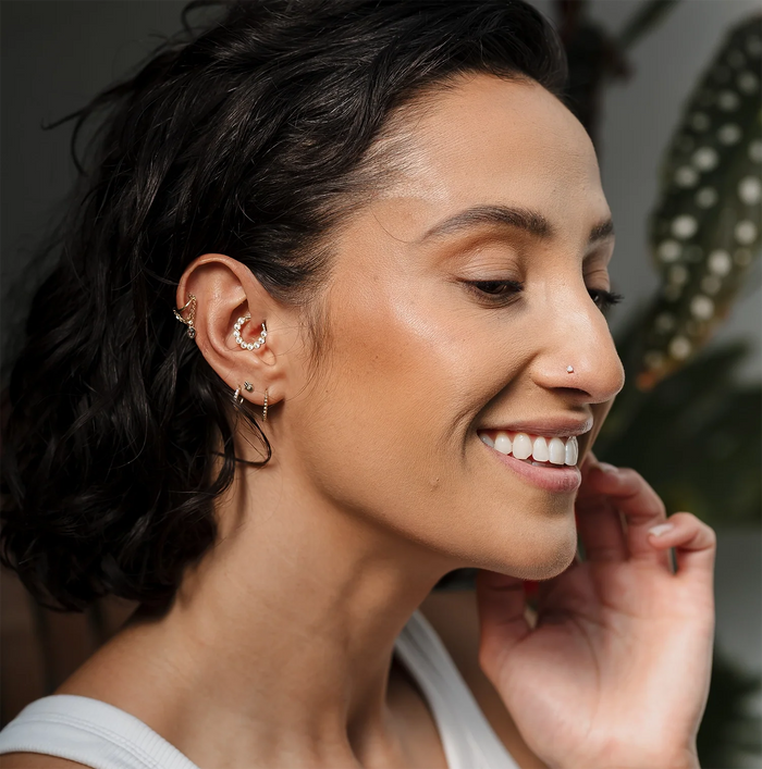 Woman wearing multiple Tish Lyon gold hoop and stud earrings on helix and lobe piercings, smiling against blurred indoor background.