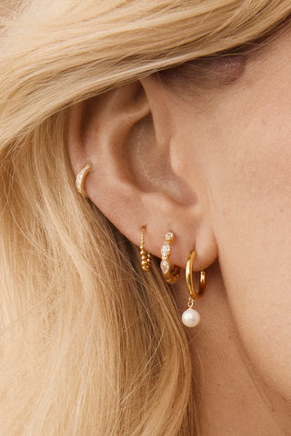 Smiling man wearing a single Tish Lyon gold hoop earring, styled with a dark shirt in natural lighting.