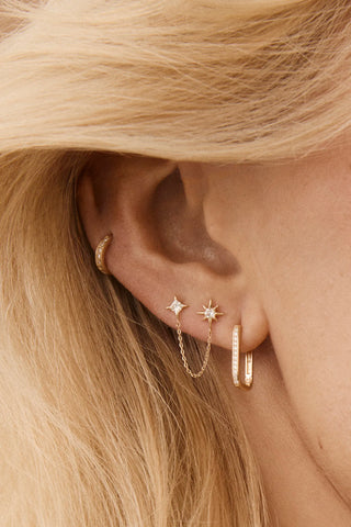 Close-up of an ear styled with multiple Tish Lyon solid gold earrings, including delicate hoops and studs with sparkling gemstones.